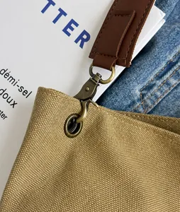 Detail of durable bronze metal hook and brown leather accent on khaki canvas bucket bag