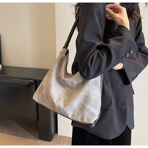 Detail of grey denim hobo bag with leather strap and chain worn by a model in a suit