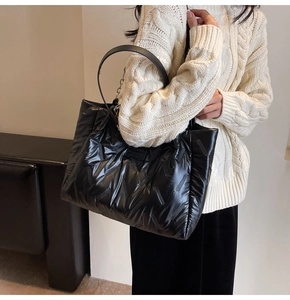 Close-up of black quilted puffer tote bag featuring silver chain and leather handle detail