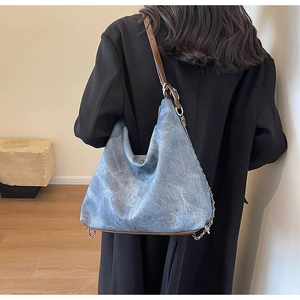Detail of blue denim hobo bag with adjustable brown leather strap and silver chain accent