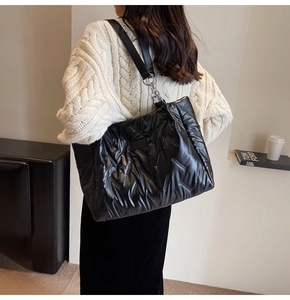 Close-up of black quilted tote bag with silver chain straps shown on shoulder
