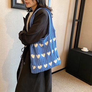 Sac fourre-tout bleu tricoté avec cœurs blancs porté sur un long manteau noir