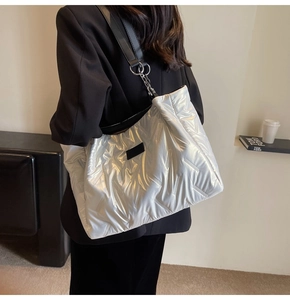Silver quilted tote bag with black strap worn by model in a modern home interior
