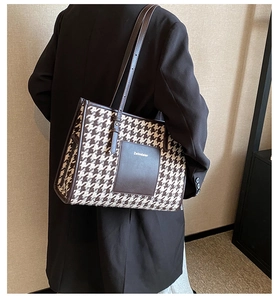 Detail of houndstooth tote bag with brown leather strap worn on shoulder by a model
