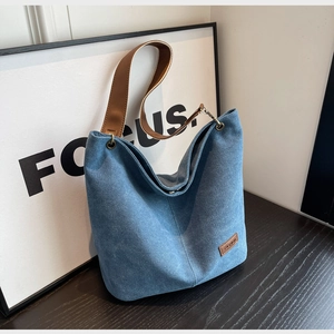 Detail of blue denim canvas bucket bag with brown leather handles and metal eyelets