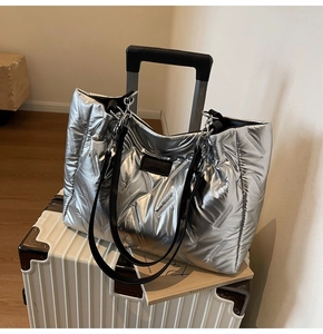 Detail of silver quilted tote bag with metallic sheen, black leather handles and chain