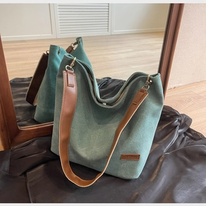 Detail of teal canvas tote bag with brown leather strap and metal hardware on silk