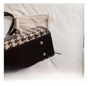 Close-up of houndstooth tote bag bottom featuring brown leather and gold metal studs
