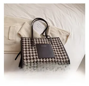 Detail of a large houndstooth tote bag with brown leather handles and brand logo