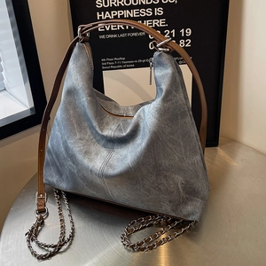 Large denim Hobo bag with chain strap and leather handle displayed on a metal table