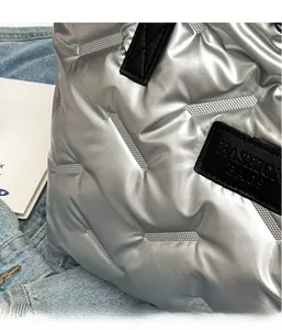 Détail du sac cabas matelassé argenté avec étiquette logo noire et surpiqûres