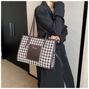 Detail view of large houndstooth tote bag featuring leather pocket and branded logo