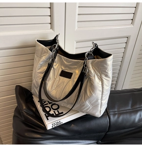 Close-up of metallic silver quilted tote bag featuring chain straps and black leather handles