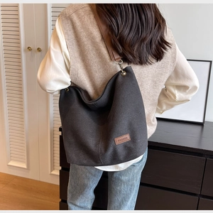 Detail of black canvas tote bag with brown leather strap and fashion label on shoulder