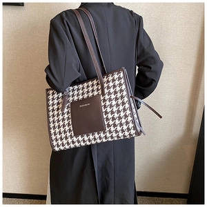 Detail of large houndstooth tote bag with brown leather straps worn over a black coat