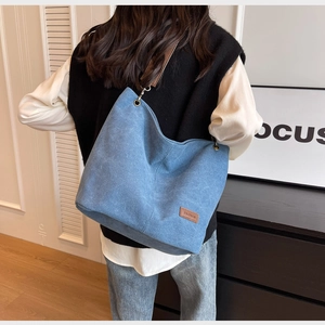 Detailed back view of a blue denim tote bag with brown leather label and wide shoulder strap