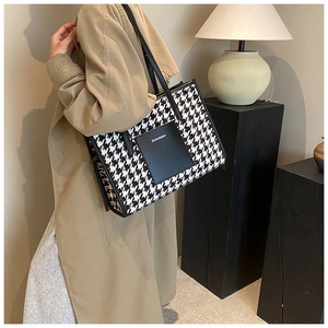 Black and white houndstooth tote bag shown on model in a cozy interior setting