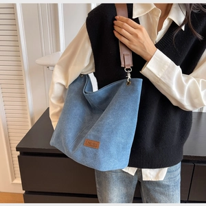 Close-up of blue canvas tote bag with brown leather FASHION patch and wide shoulder strap