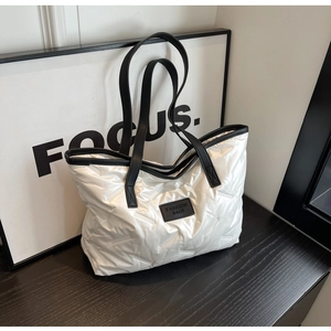 Détail du cabas matelassé blanc en tissu brillant avec étiquette de mode noire