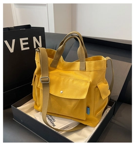 Detail of yellow canvas tote bag featuring brown top handles and front metal snap pocket