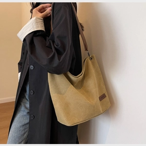 Detail of canvas bucket bag featuring a mustard yellow body and dark brown leather straps