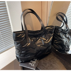 Detail of black quilted puffer tote bag with glossy finish and fashion logo label