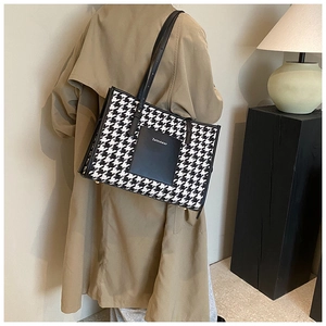 Close-up of a houndstooth tote bag with a leather logo patch on a brown trench coat