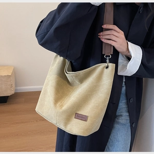 Close-up of mustard canvas bucket bag with brown leather FASHION label and metal hook