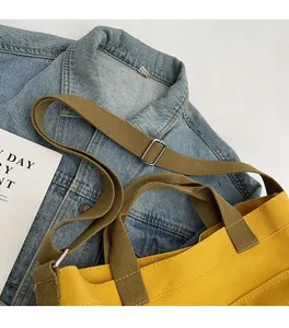 Detail of yellow canvas tote bag with adjustable brown shoulder strap and metal buckle