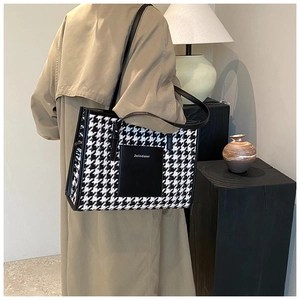 Detail of large houndstooth tote bag featuring a black leather front pocket on the side