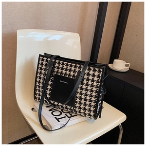Detail of black and white houndstooth tote bag with leather handles and brand patch
