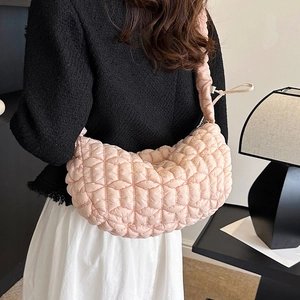 Pale pink quilted nylon crescent bag worn crossbody by model in minimalist studio