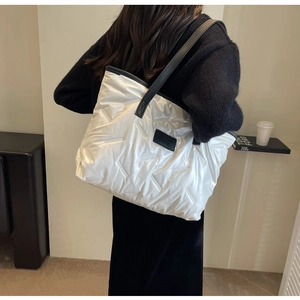 Detailed shot of white quilted down tote bag with black handles on a female shoulder