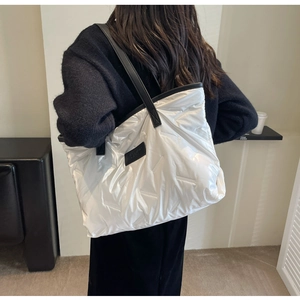 Detail of white quilted metallic tote bag with black leather straps and fashion label