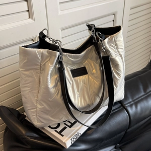 Silver quilted tote bag with black leather straps on a white book for autumn fashion