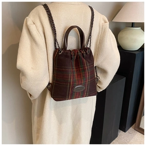 Detail eines rot-braunen Karo-Rucksacks mit Metallkette und Ledergriff im Fokus