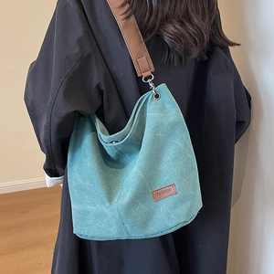 Green canvas bucket bag with wide brown strap shown on a model for casual daily style