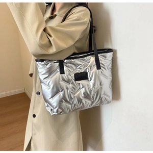 Silver quilted tote bag with metallic finish and black straps worn by a model