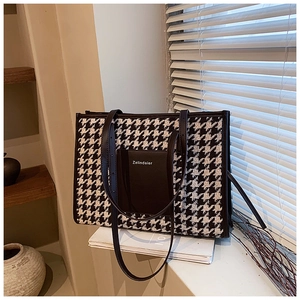 Close-up of houndstooth tote bag featuring a black leather front pocket on a magazine