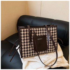 Close-up of houndstooth tote bag with brown leather brand patch on a soft fabric surface
