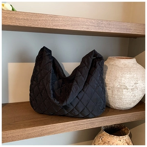 Detail of black quilted hobo tote bag with diamond stitching on a wooden shelf
