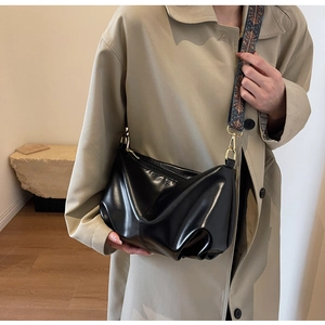 Detail of black leather dumpling bag with vintage patterned wide strap and gold hardware