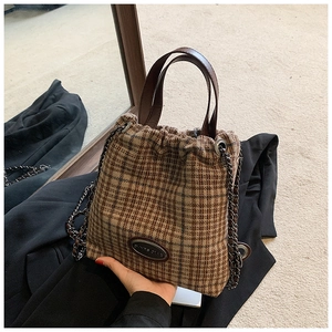 Detail der braunen Vintage-Eimertasche mit Kordelzug, Karomuster und Metallketten-Akzenten