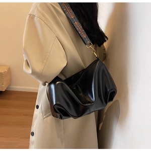Detail of black pleated cloud bag with vintage patterned wide strap on beige trench coat
