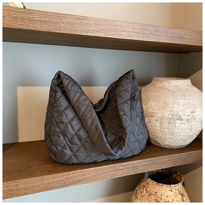 Detail of dark grey quilted nylon tote bag with rhombus stitching on a wooden shelf