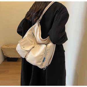 Detail der cremeweißen Nylontasche mit Seitentaschen und blauem Label an der Schulter