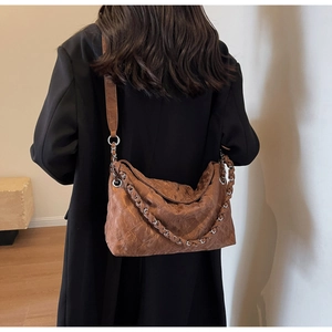 Brown quilted crossbody bag with silver chain strap shown on model's shoulder