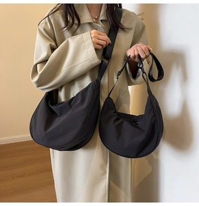 Comparison of large and small black nylon half-moon crossbody bags on a trench coat model