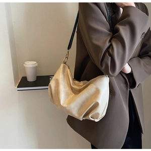 Detailed close-up of beige pleated dumpling bag with wide strap and gold hardware