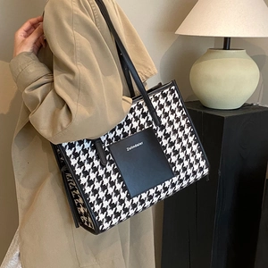 Large houndstooth tote bag with leather straps worn by a model in a trench coat